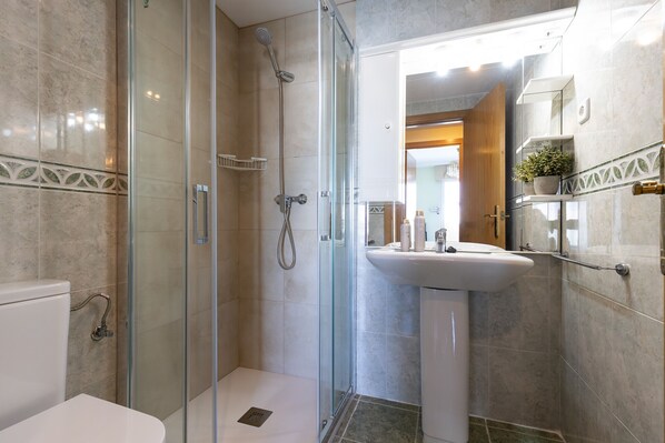 A modern bathroom with a glass-enclosed shower, a white sink, and a marble-tiled floor.