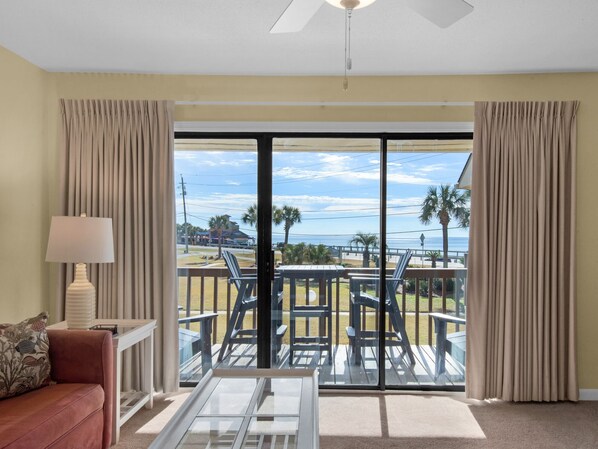 A room with a view of the beach, featuring a sofa, a table, and a lamp.