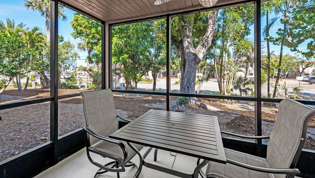 Un patio cubierto con una mesa y sillas, ventanas amplias que dan a vista de árboles y un estacionamiento.