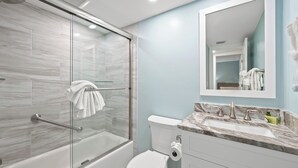 Un baño moderno con ducha envuelta en vidrio, inodoro blanco y encimera de mármol con lavabo.