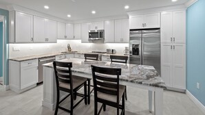 Una cocina moderna con armarios blancos, una isla de mármol y electrodomésticos de acero inoxidable.