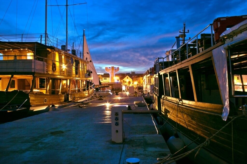 A waterfront area with boats docked, a large illuminated structure in the background, and buildings with balconies.