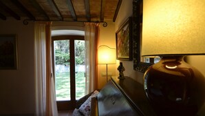 A room with a wooden ceiling, a lamp, a sofa, a door leading to a garden, and a painting on the wall. - Appartamento Valentino (Cegliolo)
