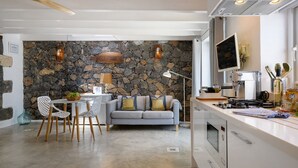 Una cocina moderna con pared de piedra, sofá gris y muebles de cocina blancos.