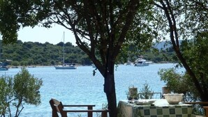 A table and chair set under a tree by a lake with boats in the background.