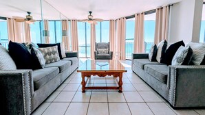 A spacious living room with two sofas, a coffee table, and ceiling fans. Large windows offer a view of the ocean. - Windward bldg at Edgewater, overlook the Sea Oats and Sand! (Panama City Beach)
