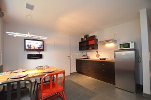 Une cuisine compacte comprenant une table à manger, des chaises, un téléviseur, un four à micro-ondes et un réfrigérateur.
