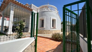 Un bâtiment blanc avec une terrasse carrelée, un portail vert et une clôture blanche.