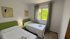 Ein Hotelzimmer mit zwei Einzelbetten, einem Nachttisch mit Lampe und einem Fenster mit Vorhängen.