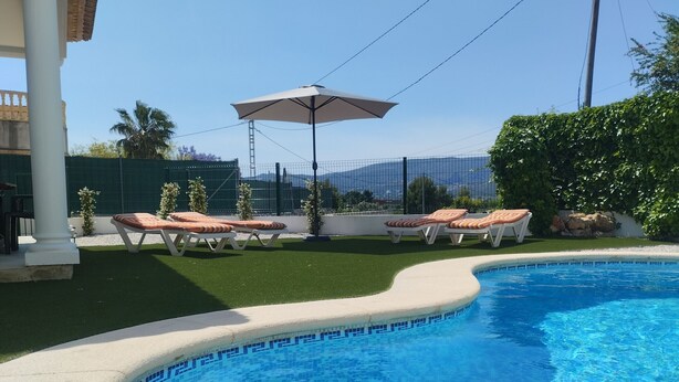 Une piscine dont les bords sont recouverts de carrelage, entourée de gazon synthétique et de chaises longues.