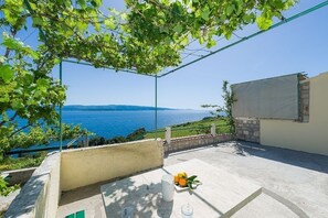 Relax on the serene outdoor terrace with a clear view of the sea, surrounded by lush greenery and a metal structure.
