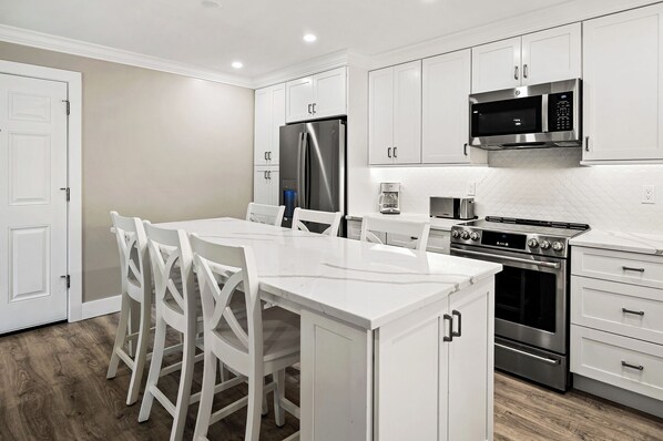 A modern kitchen with white cabinetry, a central island with chairs, a refrigerator, a microwave, and a stove. - Newly Renovated Garden View 2 bed, 2 bath at Sanibel Moorings #811 (Sanibel)