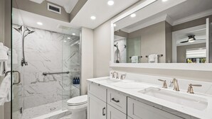 Un baño moderno con ducha de vidrio, dos lavamanos y un espejo grande.