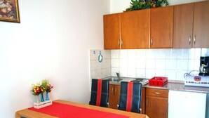 Een compacte keuken met houten kastjes, een witte koelkast en een eettafel met een rode tafelkleed.