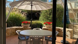 Une véranda avec une table et des chaises, un grand parasol et des plantes en pot.