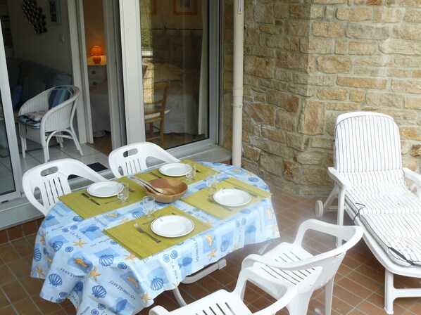 Un espace patio avec une table pour deux personnes, des chaises en plastique blanches et un mur en pierre.