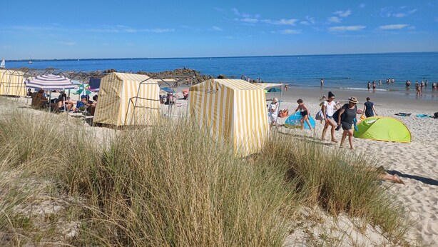 Une plage avec des tentes et des personnes qui se prélassent au soleil.