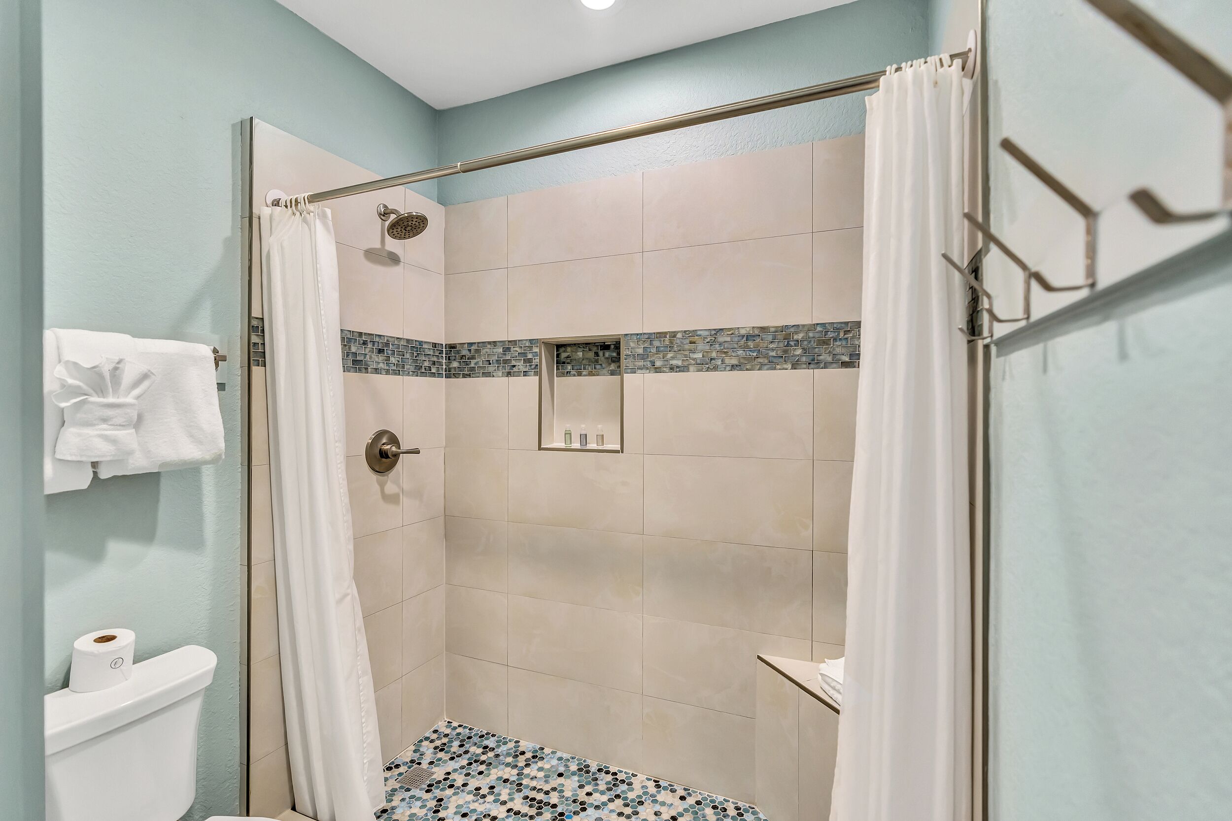 A shower area with a glass door, a white towel on the wall, and a tiled floor.