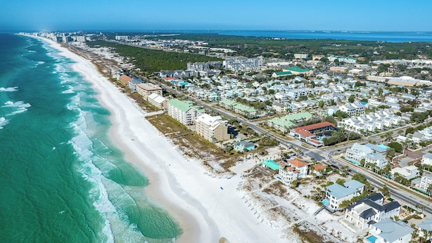 An aerial view of a coastal town with a wide sandy beach, residential buildings, and a clear view of the ocean. - Spend Time with Your Family and Dog at the Beachside Inn Hotel! (Destin)