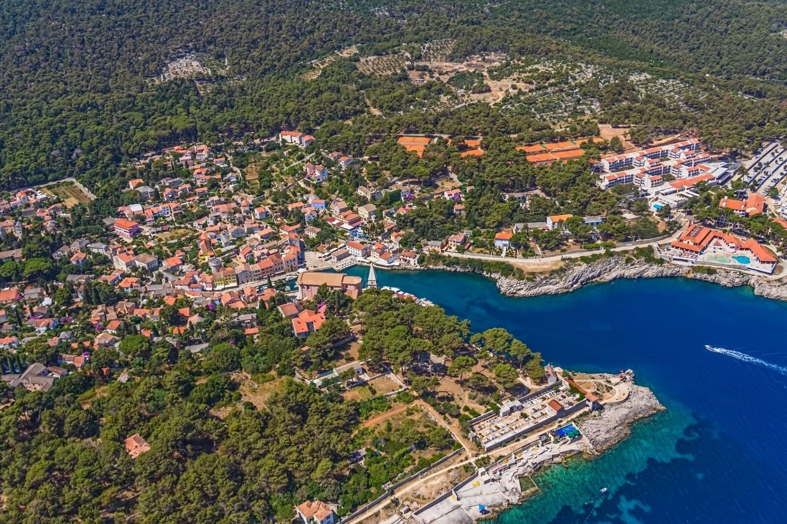 An aerial view of a coastal town with residential buildings, a marina, and a rocky coastline.