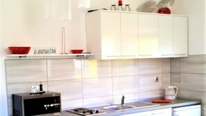 Cozinha moderna com armários brancos, pia de aço inoxidável e um banco de balcão vermelho.