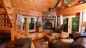 A wooden cabin interior with a fireplace, leather sofas, a TV, and a stone wall. - Shady Lady Cabin in The Smokies with Beautiful Views, Just 5 miles from Town (Sevierville)
