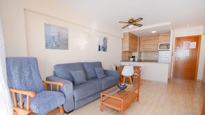 A living room with a sofa, a chair, a coffee table, and a kitchen area with cabinets and appliances. - A59 CALPEMAR A 5º 18 (Calpe)