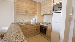 A kitchen with wooden cabinets, a granite countertop, a built-in oven, and a refrigerator. - A59 CALPEMAR A 5º 18 (Calpe)