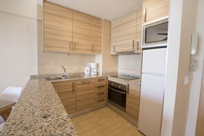 A kitchen with wooden cabinets, a granite countertop, a built-in oven, and a refrigerator. - A59 CALPEMAR A 5º 18 (Calpe)