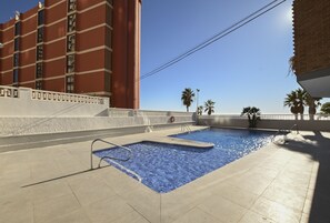A rooftop swimming pool with clear blue water, surrounded by a white wall and a tall red building. - A59 CALPEMAR A 5º 18 (Calpe)