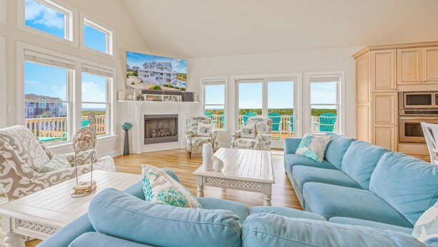 Un salon spacieux avec un grand canapé bleu, une cheminée et une vue sur une propriété située en bord de mer.