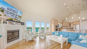 Un salon spacieux doté d’une cheminée, d’un grand canapé et offrant une vue sur l’océan grâce à de grandes fenêtres.