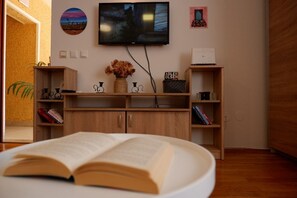 Une pièce avec une bibliothèque en bois, un téléviseur fixé au mur et un grand livre ouvert sur une table blanche.
