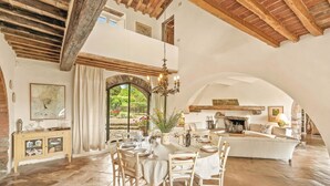 A spacious dining area with a high ceiling, a fireplace, and a view of a garden through an arched window. - Villa in Lucarelli with 6 bedrooms sleeps 10 (Lucarelli)