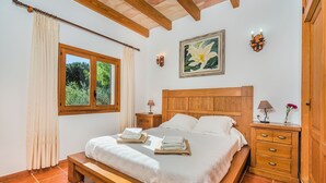 A bedroom with a wooden bed, a nightstand with a lamp, a wooden dresser, and a window with curtains. - BLANCO  Ref. VP08 (Pollensa / Pollença)