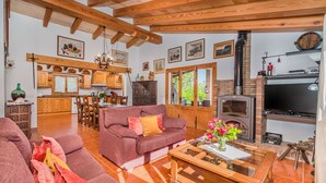 A spacious living area with a wooden ceiling, a fireplace, a television, and a kitchen in the background. - BLANCO  Ref. VP08 (Pollensa / Pollença)
