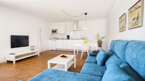 Un salon moderne avec un canapé bleu, une table basse blanche et un téléviseur à écran plat.