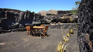 Un espace extérieur aménagé avec une table et des chaises, entouré de roches volcaniques et d’une végétation clairsemée.
