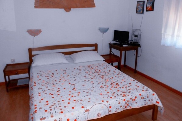 A bedroom with a wooden bed, a desk with a computer, and a wall-mounted lamp.