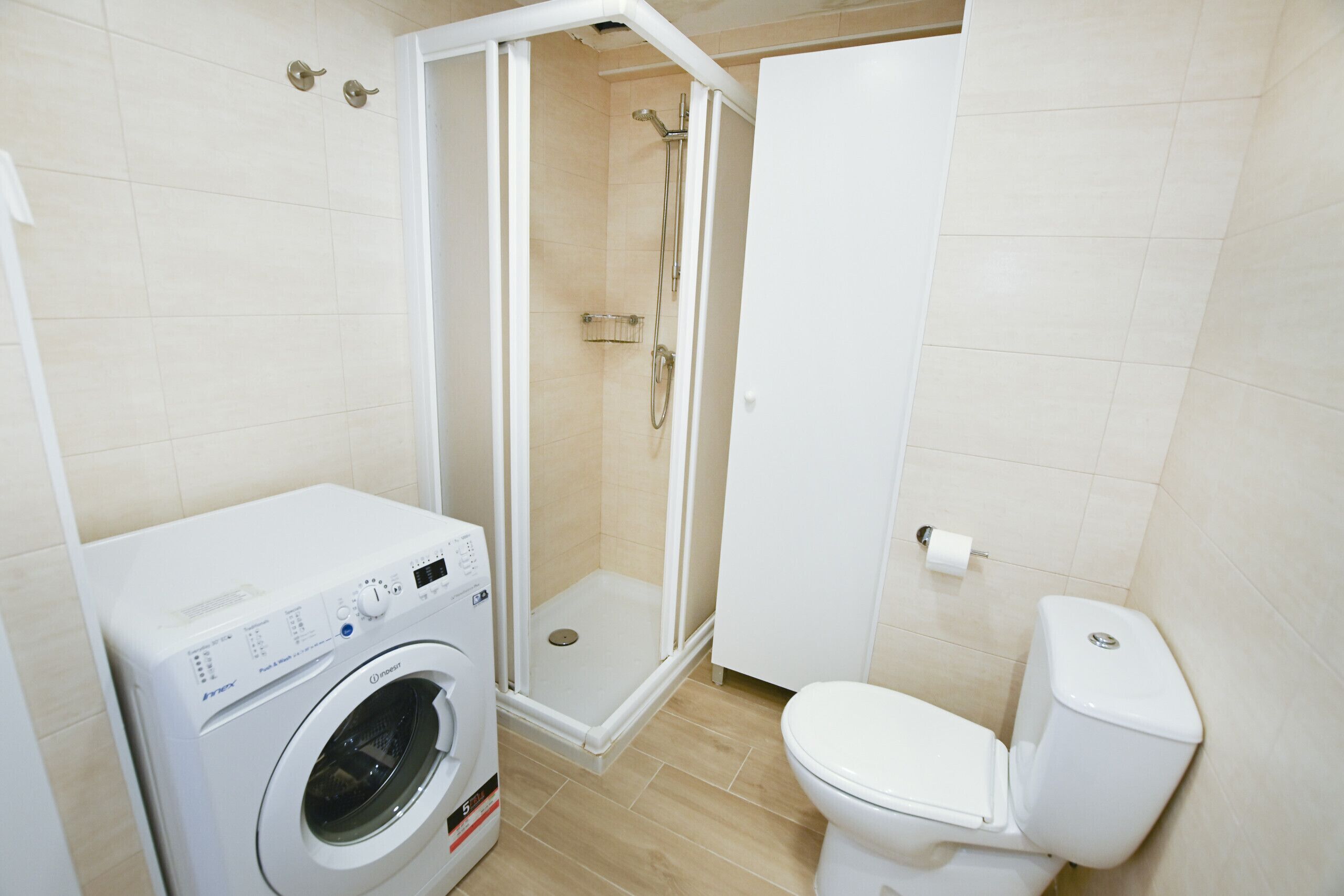 A bathroom with a washing machine, a toilet, and a shower enclosure.