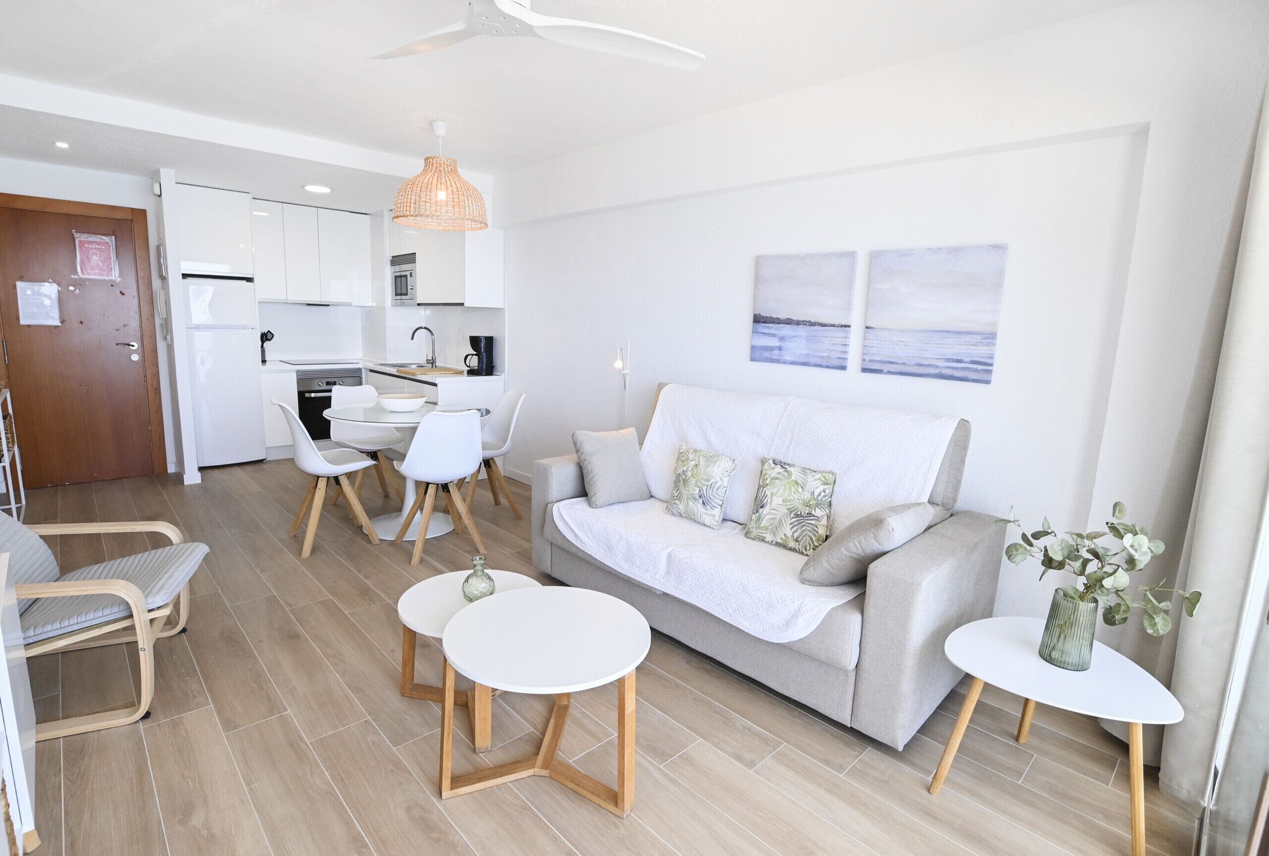 A modern living room with a sofa, two white tables, and a dining area with chairs.
