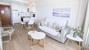 Ein modernes Wohnzimmer mit einer Couch, zwei weißen Tischen und einem Essbereich mit Stühlen.