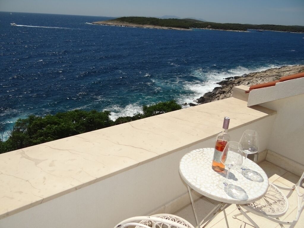 A balcony with a table and chairs overlooking a coastal view.