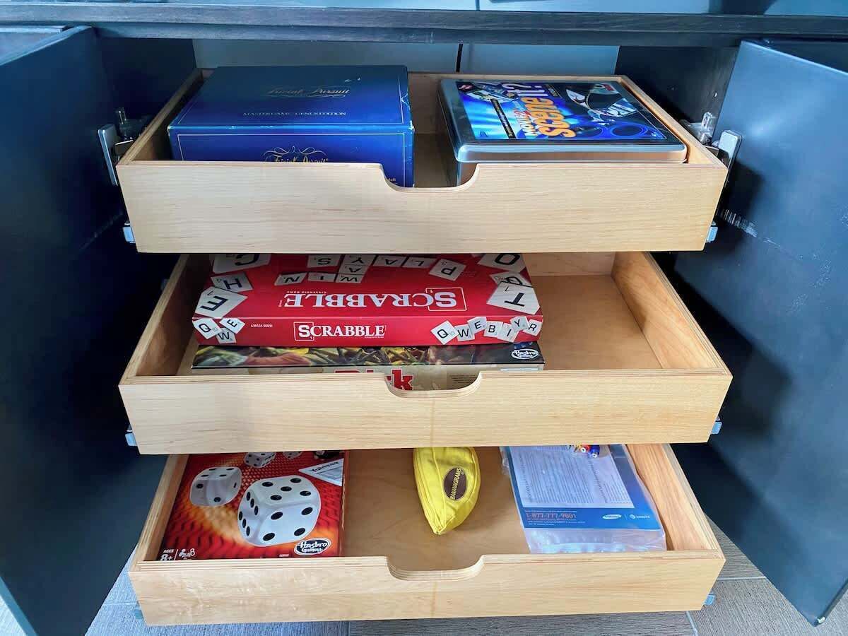 Un tiroir divisé en trois compartiments contenant un jeu de Scrabble, un téléphone intelligent et des dés.