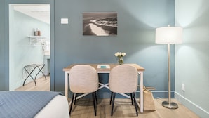 Ein Hotelzimmer mit einem Bett, einem Schreibtisch mit zwei Stühlen, einer Schreibtischlampe, einem gerahmten Bild an der Wand und einem kleinen Tisch mit Blumen.