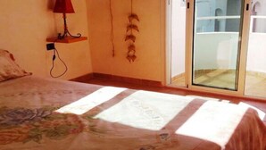A bedroom with a bed, a nightstand, a lamp, and a view of the outside through a glass door. - Nice Duplex in Sidi Bouzid 4381 (Sidi Bouzid)