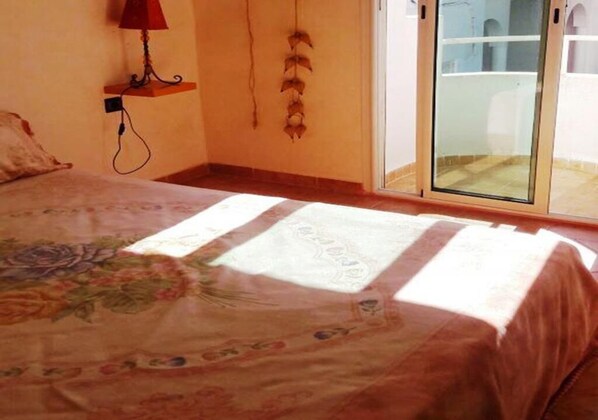 A bedroom with a bed, a nightstand, a lamp, and a view of the outside through a glass door.