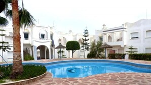 A swimming pool with a stone pathway, surrounded by white buildings with arches and a palm tree. - Nice Duplex in Sidi Bouzid 4381 (Sidi Bouzid)