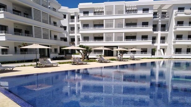Un hôtel moderne doté d’une grande piscine, de nombreux balcons et de chaises longues.