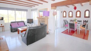 A spacious living room with a fireplace, a sofa, a television, and a dining area with chairs and a table. - Anna - Javea, Costa Blanca (Javea)